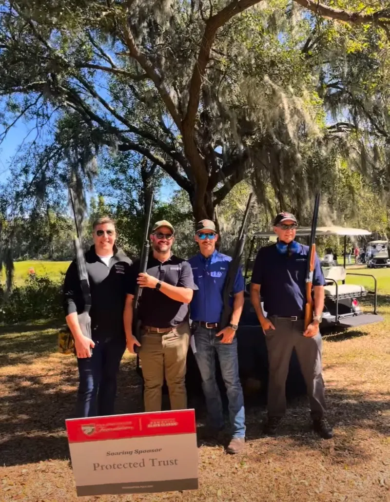 Four shooters under the oak with the Soaring Sponsor sign at the Clays Classic
